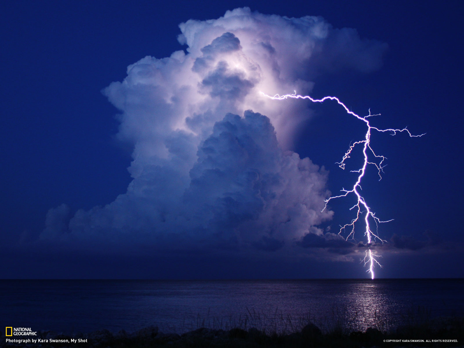 An action shot of lightning stricking the ocean while illuminating a cloud